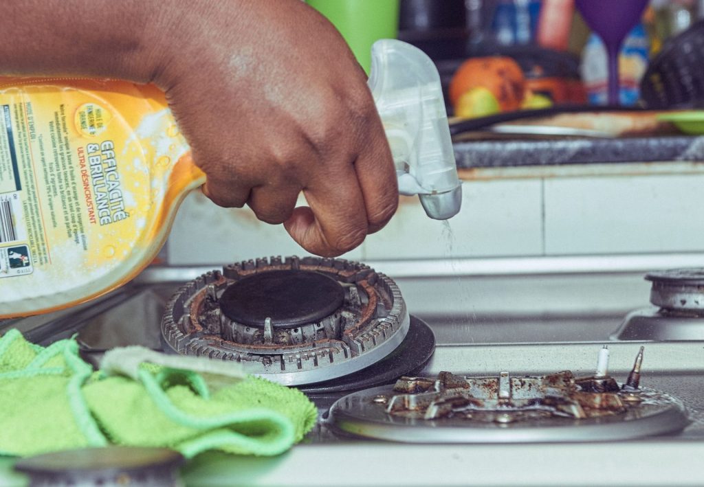 Cleaner scrubbing a gas stovetop during a deep clean